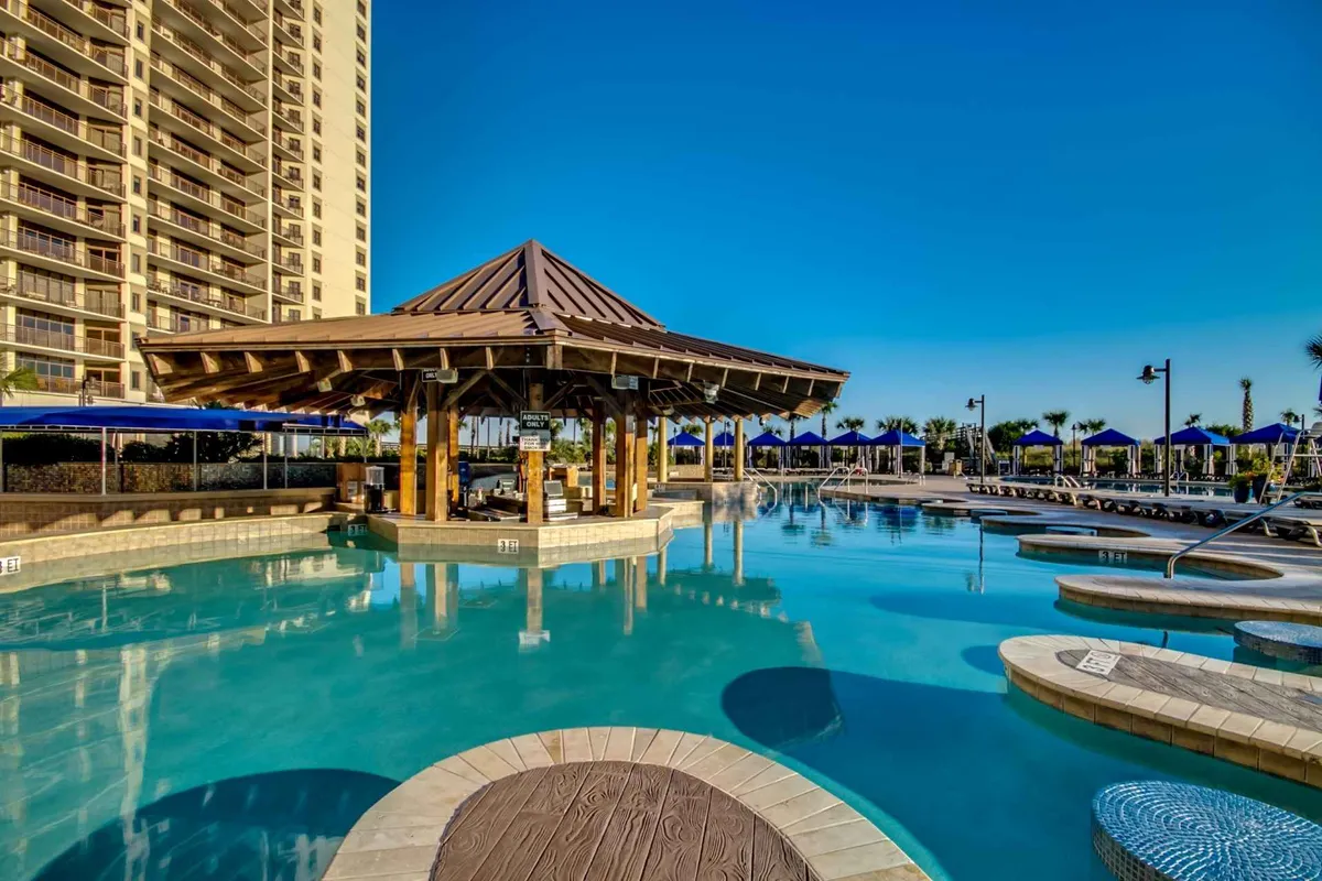 An inviting exterior pool area with a sparkling swimming pool, poolside cabana, plush lounge chairs, and tall palm trees under a cheerful sky. The setting evokes leisure and carefree poolside enjoyment.