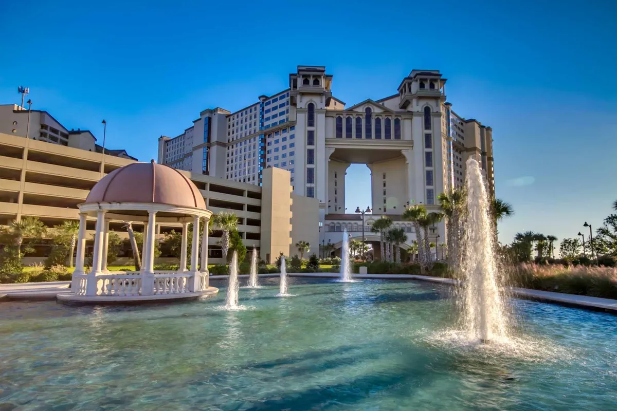 The tranquil exterior of a resort property, featuring a graceful water fountain, a charming gazebo, and the elegant architecture of the hotel structure. The lush landscaping and inviting seating areas emphasize a relaxing, upscale atmosphere.