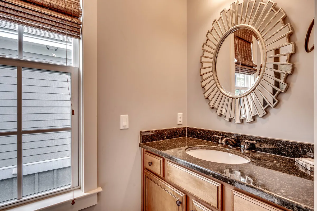 A serene bathroom interior with a large mirror, granite countertop, and a window letting in natural light, evoking calm and relaxation.