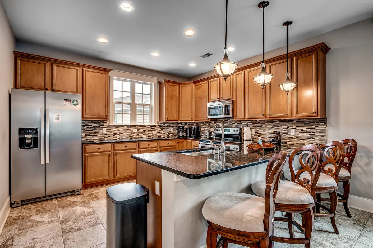 A warmly lit kitchen with granite countertops, wooden cabinets, pendant lighting, and stools at the island. The layout encourages both meal preparation and casual dining, with plenty of space for guests to gather around.