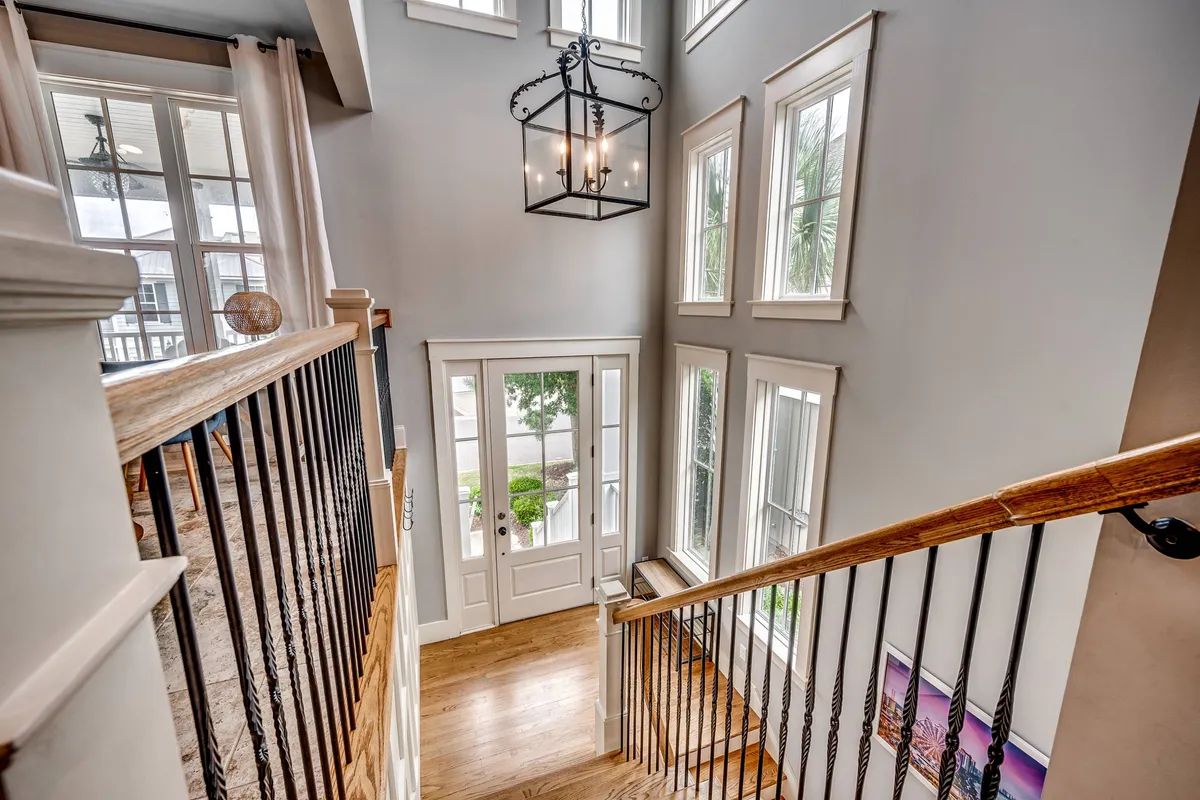 A bright, inviting entryway with a sweeping staircase, elegant chandelier, and large windows flooding the space with natural light. The entrance suggests a warm welcome and sets an upscale tone for the property.